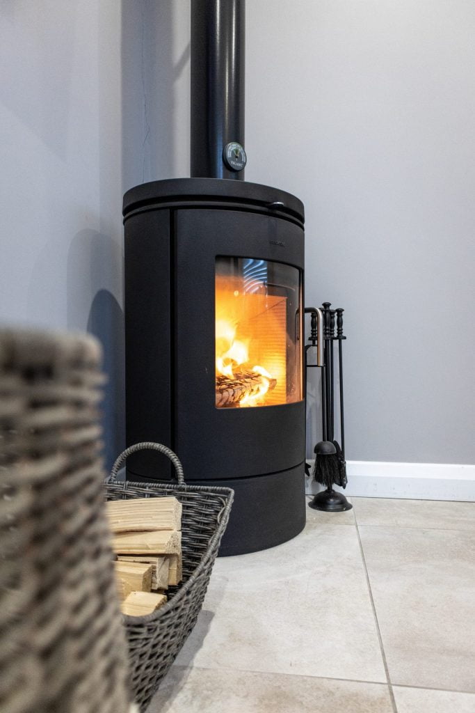 A beautiful tall round black wood burning stove in the corner of a room on a tiled floor